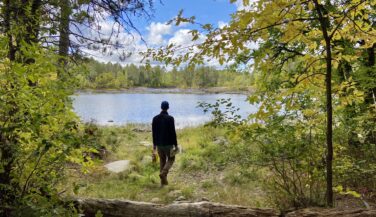 A slender man gazes out towards a BWCA lake as he walks towards it. Photo by Amy Marty.